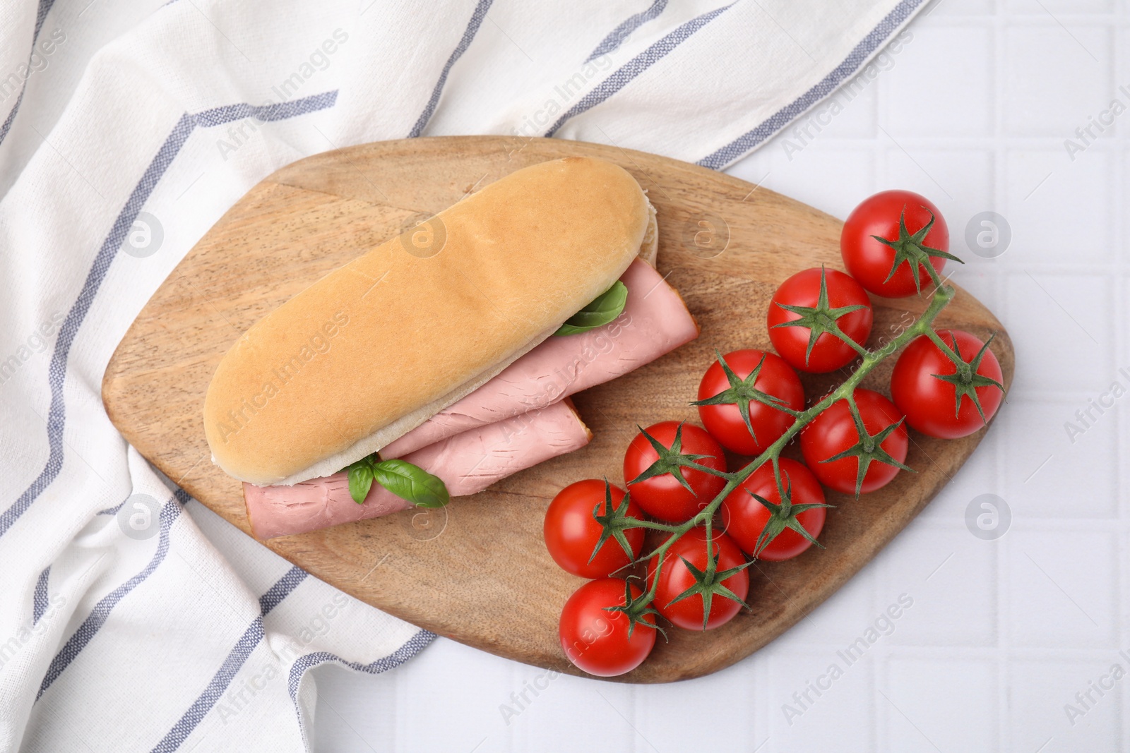 Photo of Delicious sandwich with ham, basil and tomatoes on white tiled table, top view