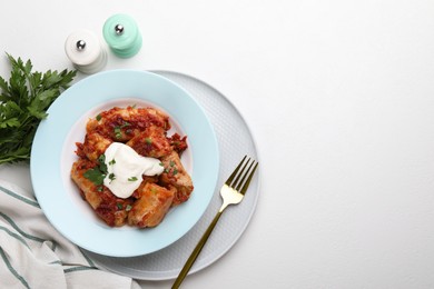 Delicious stuffed cabbage rolls served with sour cream on white table, flat lay. Space for text
