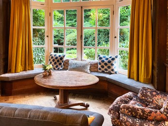 Photo of Wooden table near bay window seat with cushions in cozy room. Interior design