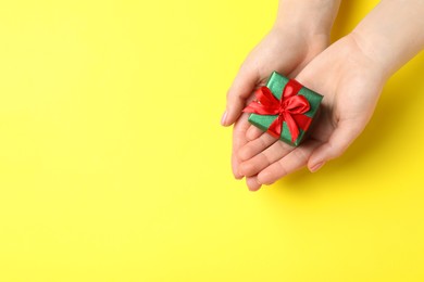 Photo of Woman holding beautifully wrapped Christmas gift box on yellow background, top view. Space for text