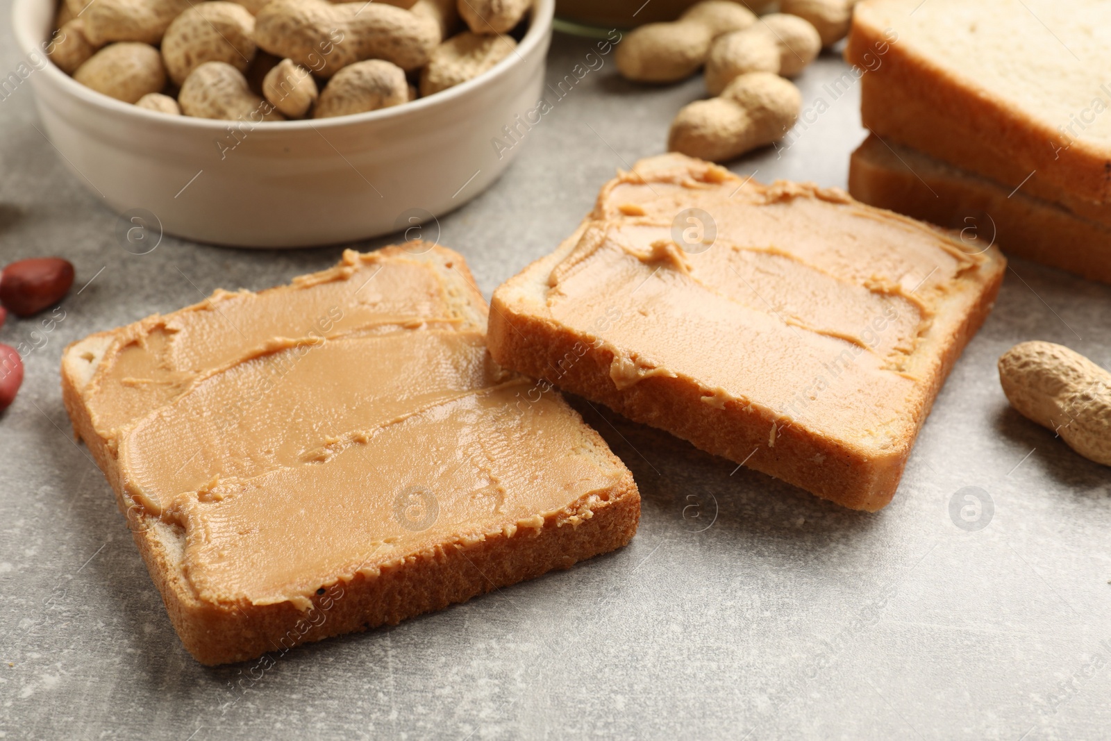 Photo of Tasty peanut butter sandwiches and peanuts on gray table, closeup