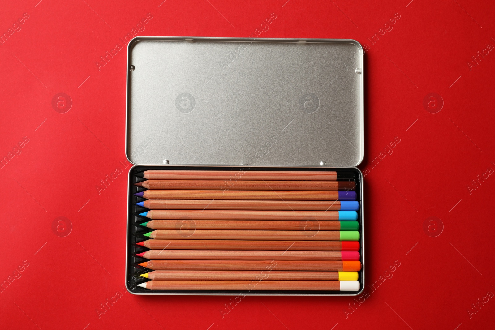Photo of Box with many colorful pastel pencils on red background, top view. Drawing supplies