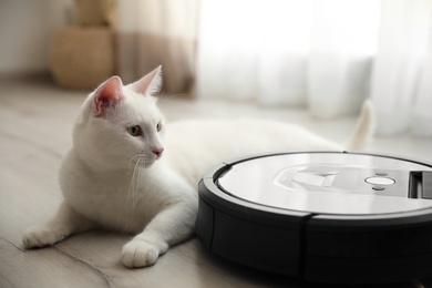 Modern robotic vacuum cleaner and cute cat on floor indoors