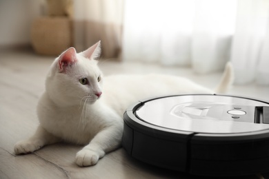 Photo of Modern robotic vacuum cleaner and cute cat on floor indoors