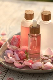Photo of Bottles of rose essential oil and flowers on white wooden table, closeup