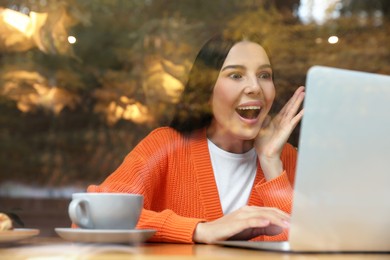 Special Promotion. Emotional young woman using laptop in cafe, view from outdoors