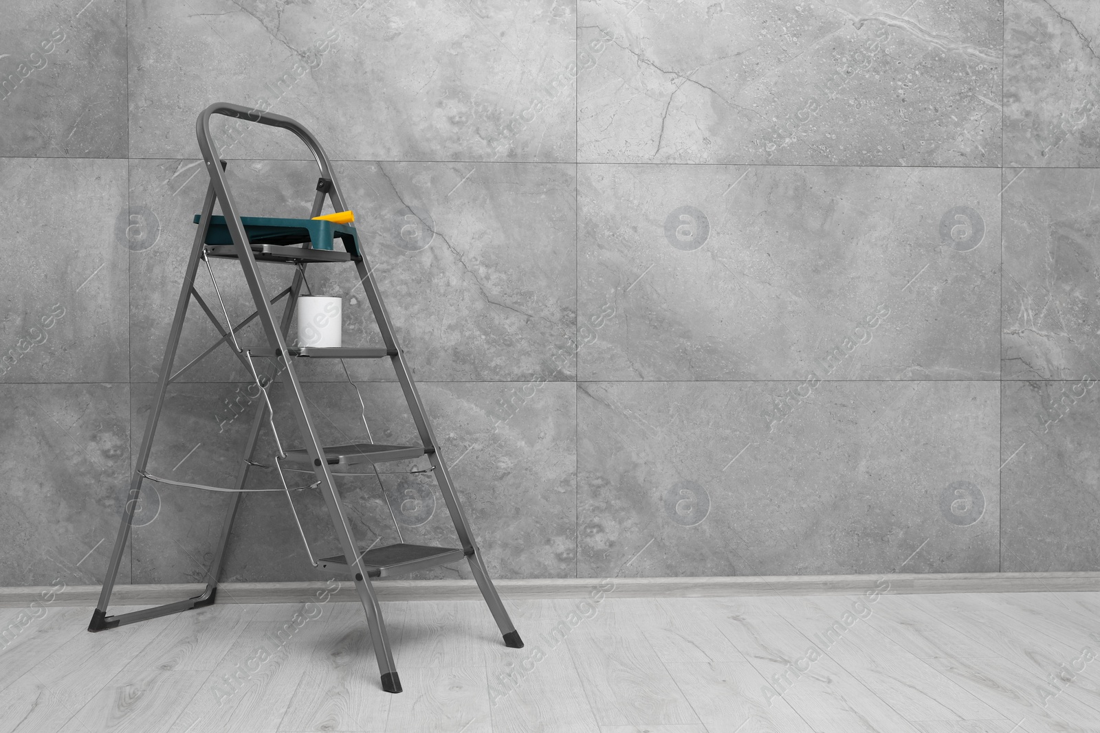 Photo of Metallic folding ladder and painting tools near grey wall indoors, space for text
