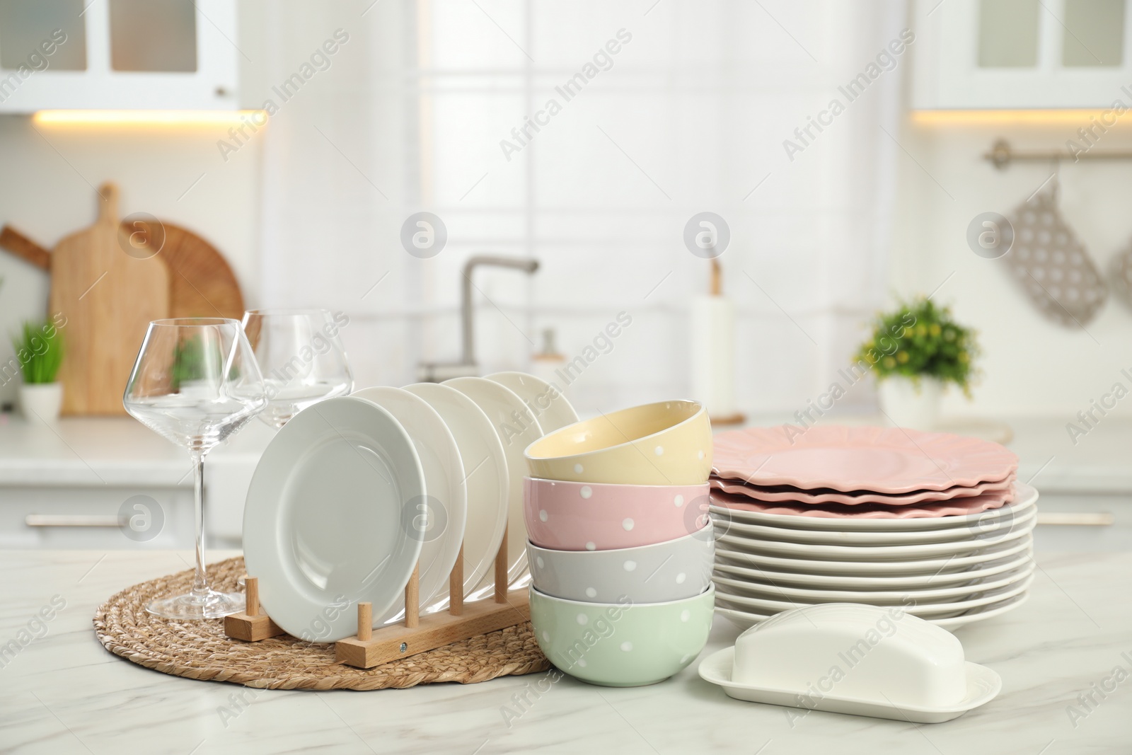 Photo of Clean plates, bowls, butter dish and glasses on white marble table in kitchen