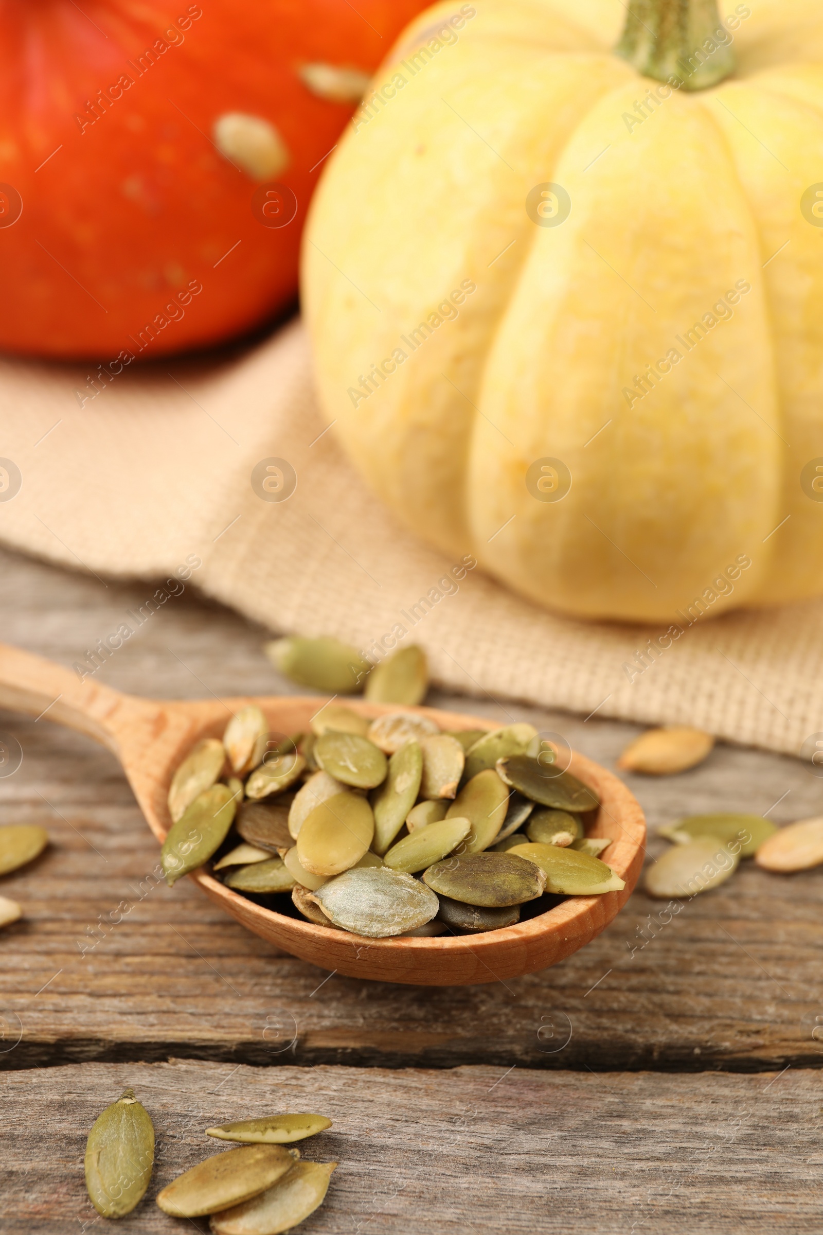 Photo of Spoon with peeled seeds and fresh pumpkins on wooden table
