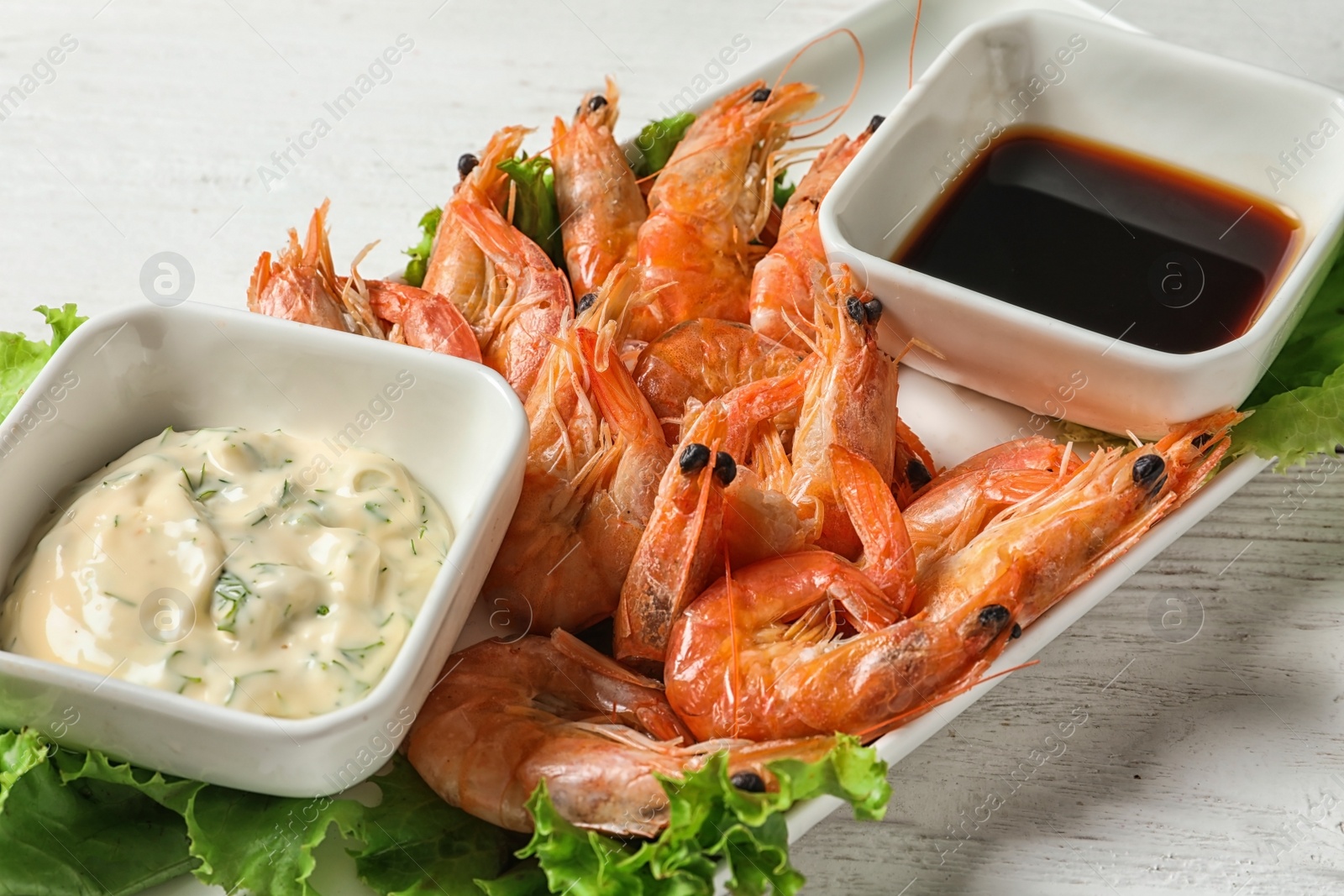 Photo of Plate with juicy shrimps and sauces on table, closeup