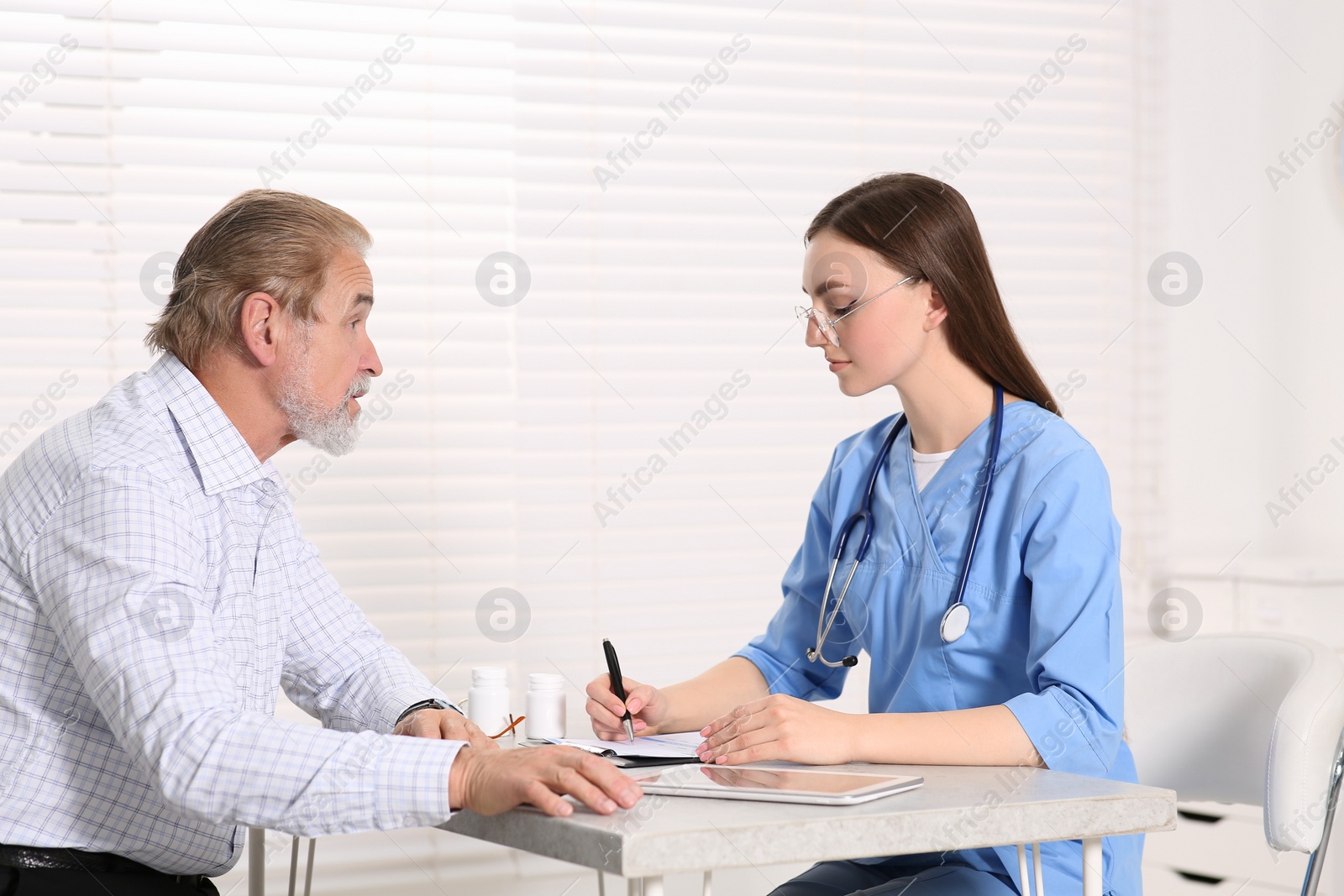 Photo of Doctor filling patient's medical card at table in clinic