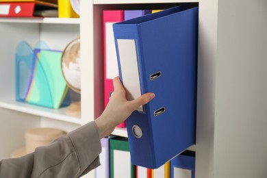 Photo of Woman taking binder office folder from shelving unit indoors, closeup