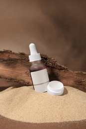 Cosmetic products and tree bark on sand against brown background