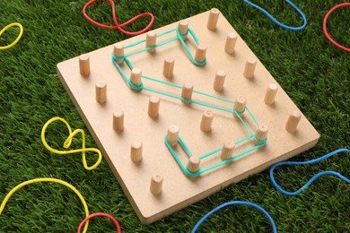 Wooden geoboard with letter S made of rubber bands on artificial grass. Educational toy for motor skills development