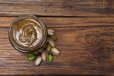 Tasty pistachio nut paste in jar on wooden table, top view. Space for text