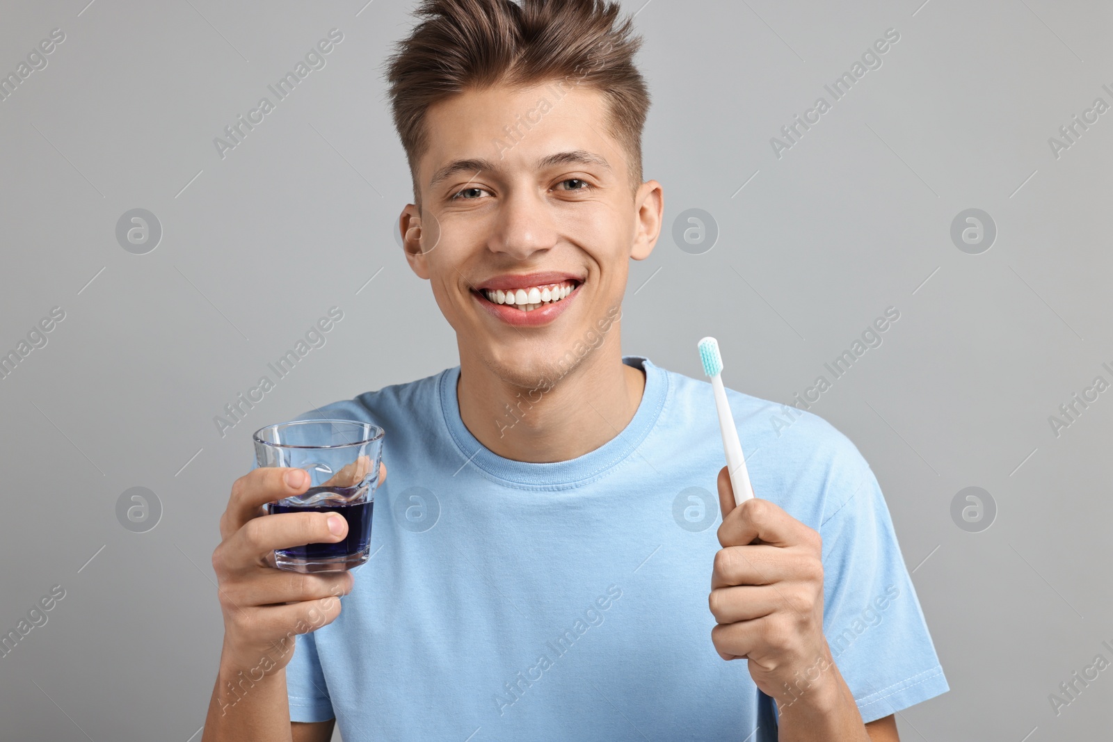 Photo of Young man with mouthwash and toothbrush on light grey background