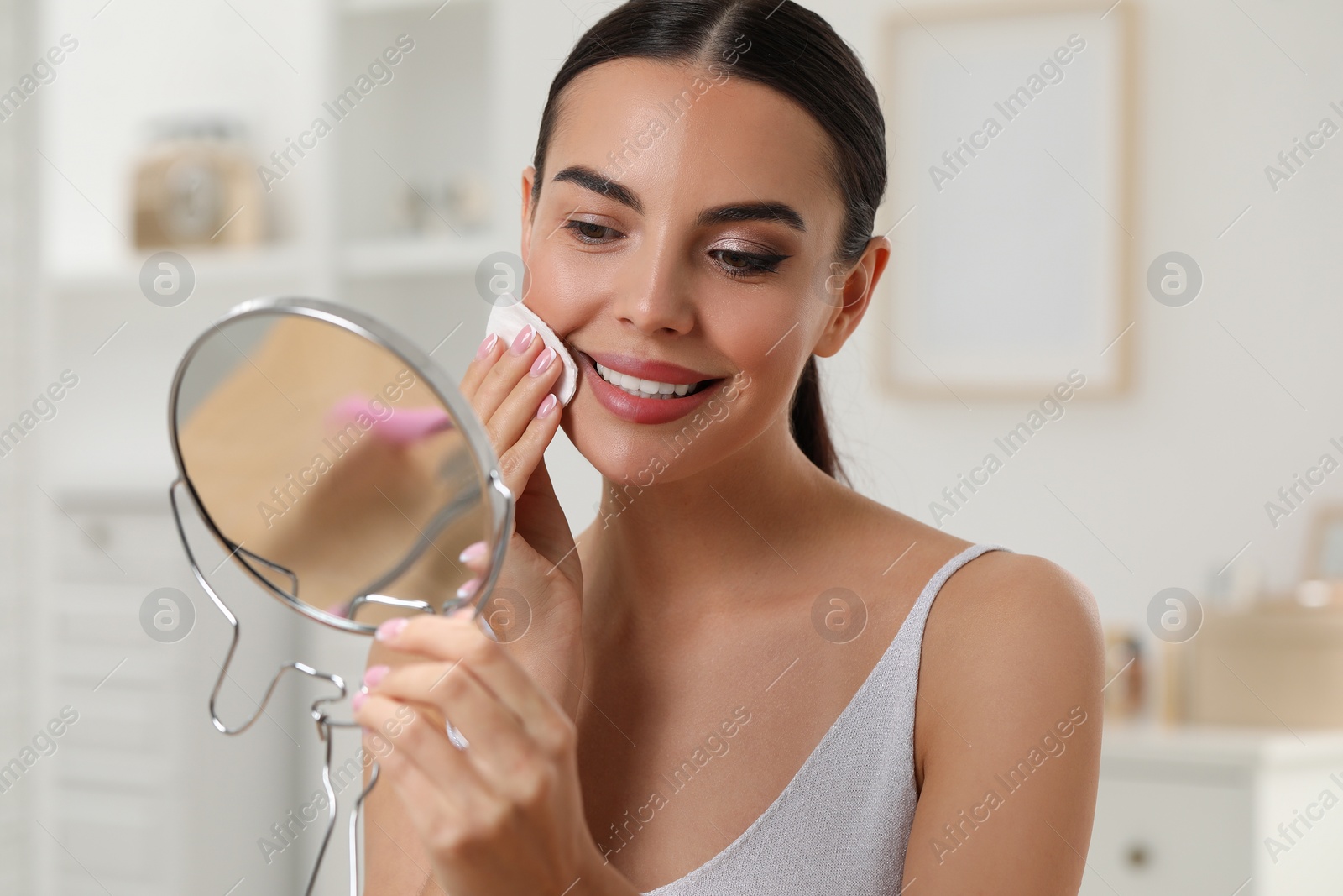 Photo of Beautiful woman removing makeup with cotton pad in room