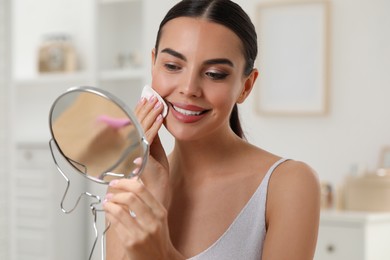 Photo of Beautiful woman removing makeup with cotton pad in room