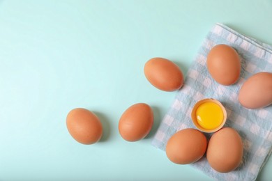 Photo of Cracked and whole chicken eggs with napkin on light blue background, flat lay. Space for text