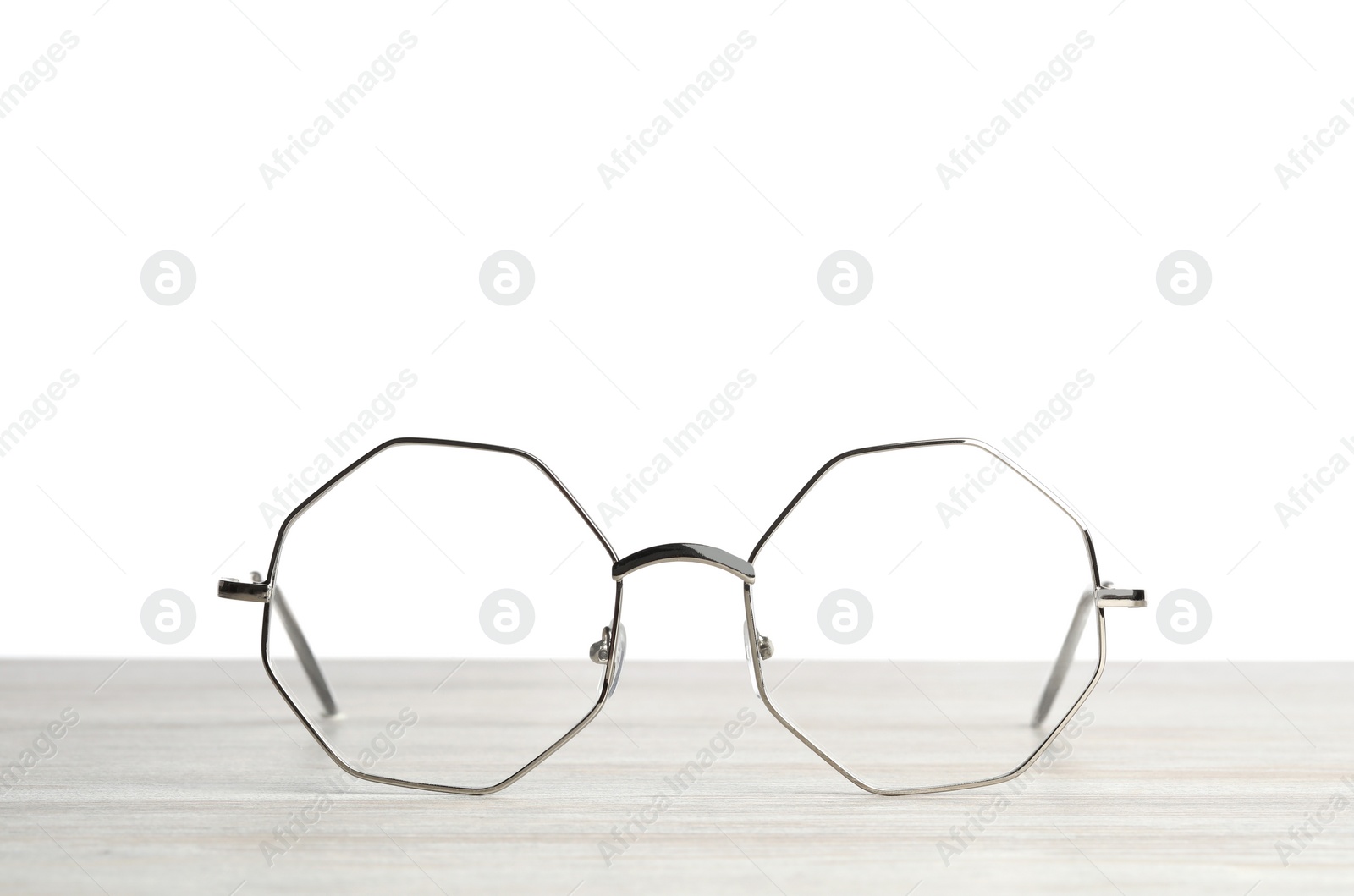 Photo of Stylish glasses with metal frame on wooden table against white background