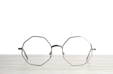 Stylish glasses with metal frame on wooden table against white background