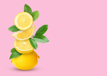 Stacked cut and whole lemons with green leaves on pale pink background, space for text
