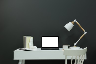 Photo of Stylish workplace with laptop, lamp, cup and decor on white table near grey wall