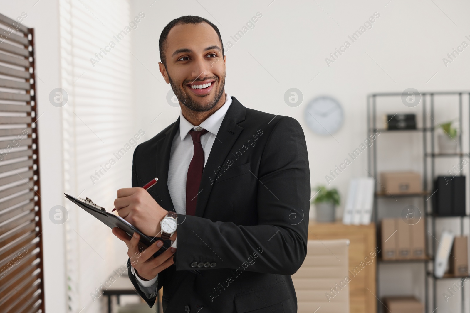 Photo of Smiling young man with clipboard writing notes in office. Lawyer, businessman, accountant or manager