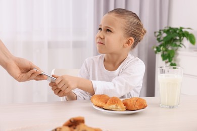 Woman taking away smartphone from her daughter at table indoors, closeup. Internet addiction