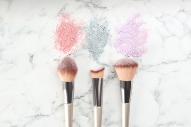 Makeup brushes and scattered eye shadows on white marble table, flat lay