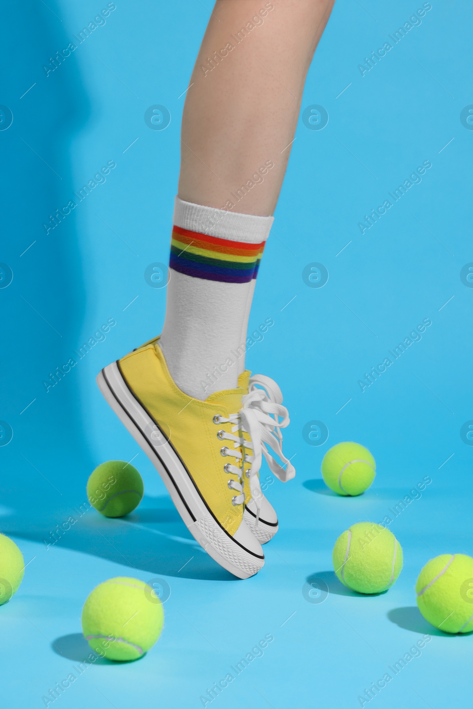Photo of Woman posing in yellow classic old school sneakers and tennis balls on light blue background, closeup