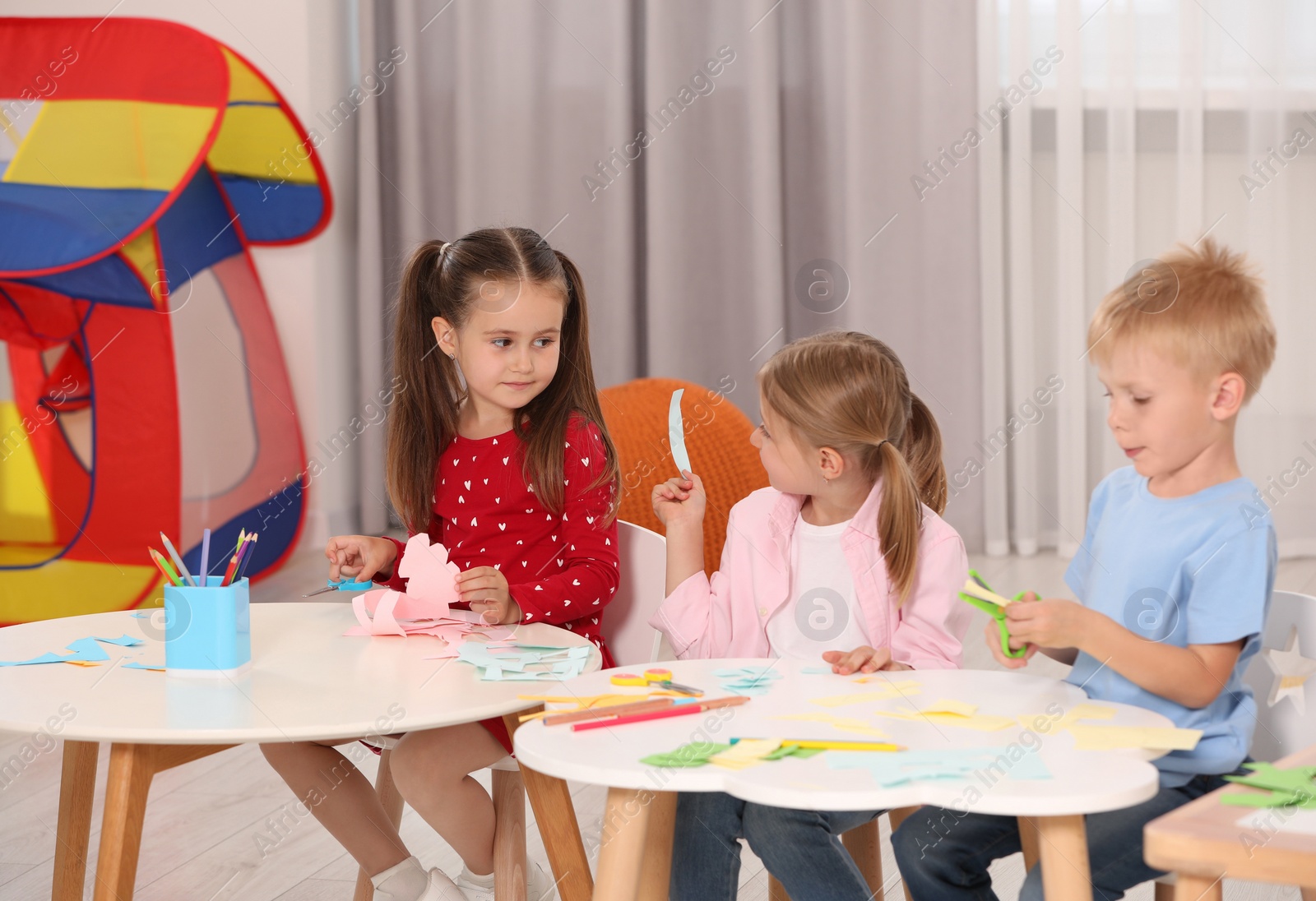 Photo of Group of cute little children making toys from color paper at desks in kindergarten. Playtime activities