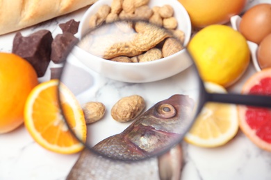 Photo of Different products with magnifier focused on fish and peanuts, closeup. Food allergy concept