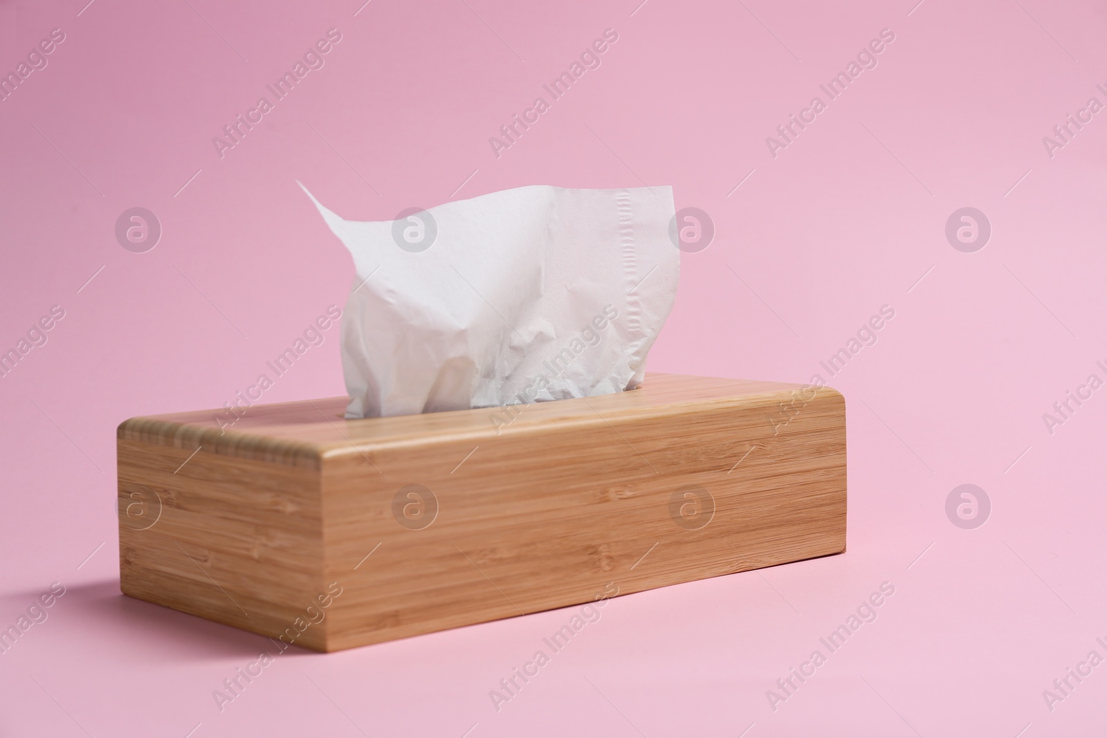 Photo of Wooden holder with paper tissues on pink background