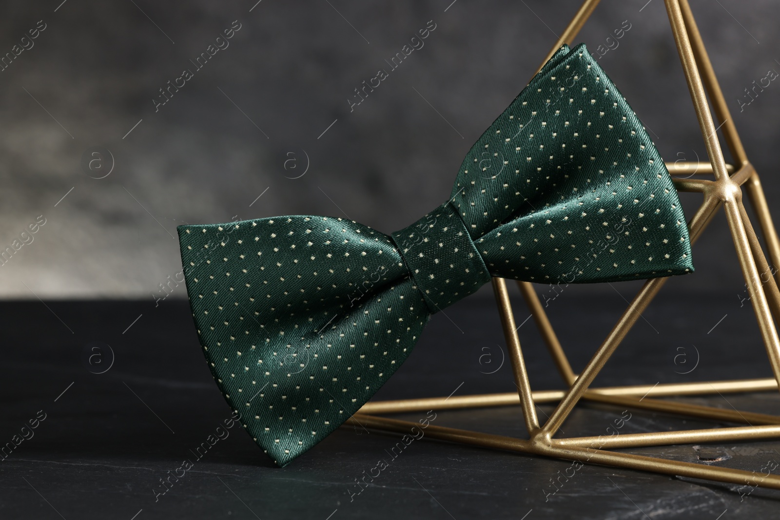Photo of Stylish presentation of green bow tie on black table against gray background