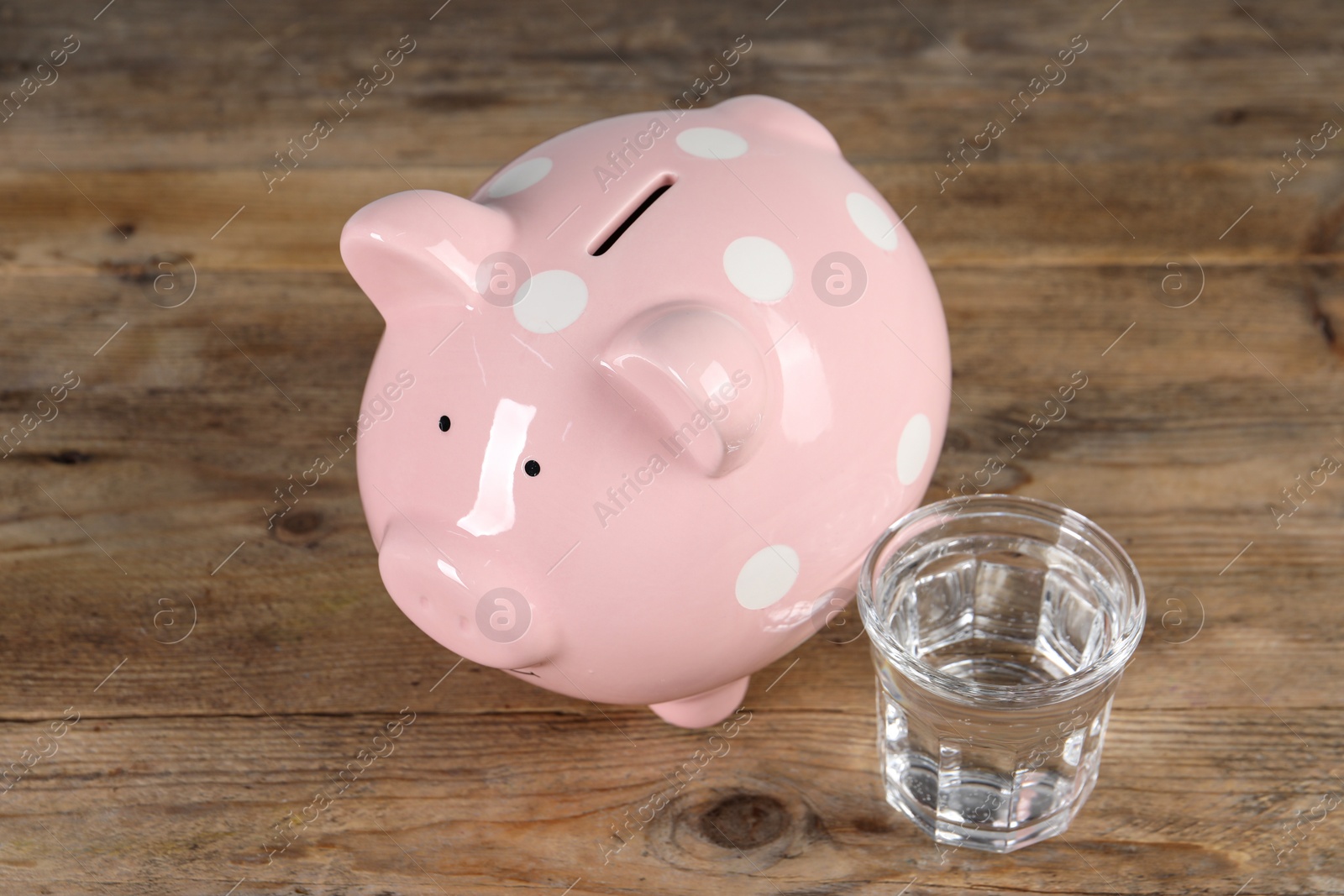 Photo of Water scarcity concept. Piggy bank and glass of drink on wooden table