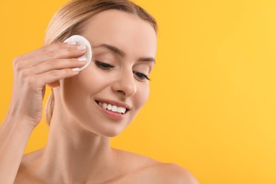 Photo of Smiling woman removing makeup with cotton pad on yellow background, closeup. Space for text