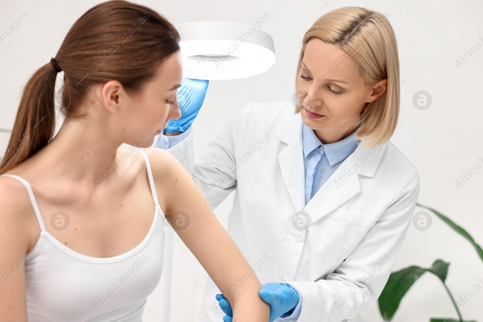 Photo of Dermatologist examining patient under lamp in clinic