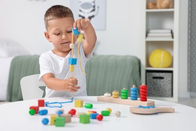 Photo of Motor skills development. Little boy playing with wooden pieces and string for threading activity at white table indoors