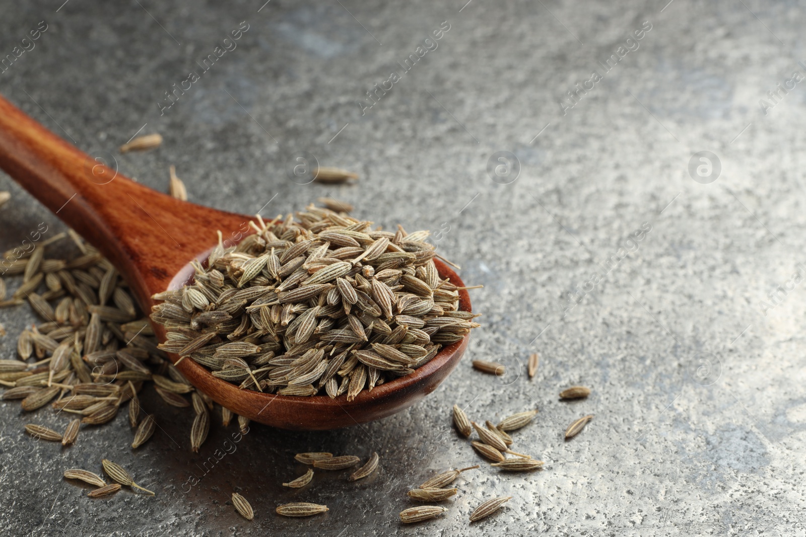 Photo of Spoon with caraway seeds on grey table, closeup. Space for text