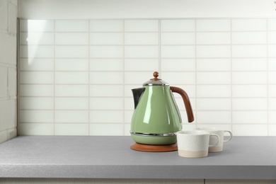 Photo of Stylish electric kettle and tea cups on grey table against white wall, space for text