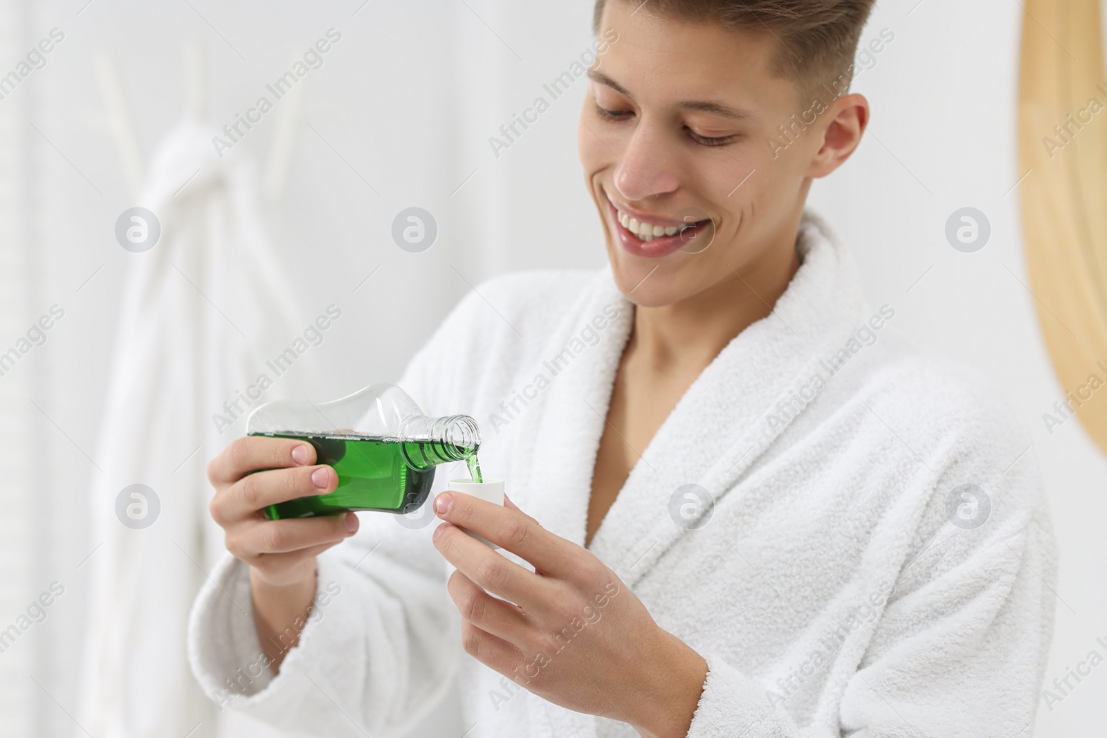 Photo of Young man using mouthwash in bathroom. Oral hygiene