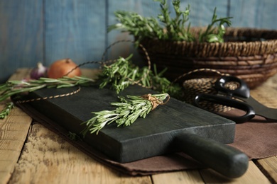 Photo of Wooden board with rosemary on table. Aromatic herbs