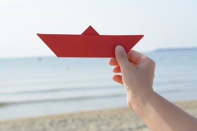 Photo of Child holding red paper boat near sea, closeup