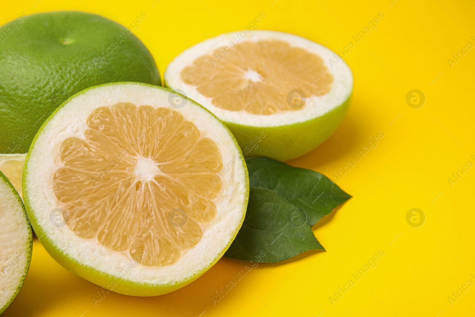 Photo of Whole and cut sweetie fruits with green leaves on yellow background, closeup. Space for text