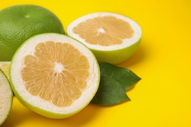 Photo of Whole and cut sweetie fruits with green leaves on yellow background, closeup. Space for text