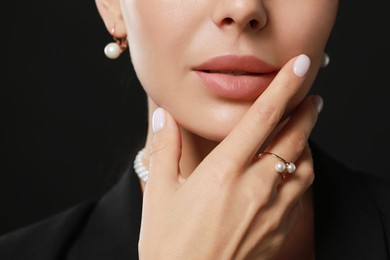 Young woman with elegant pearl jewelry on black background, closeup