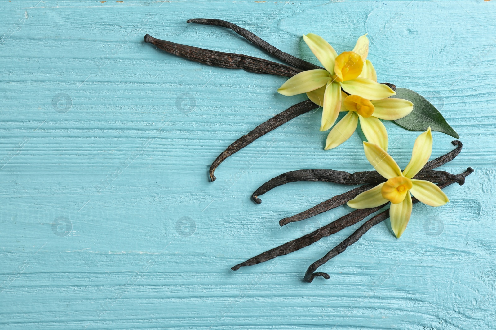 Photo of Flat lay composition with vanilla sticks and flowers on wooden background. Space for text