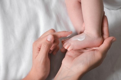 Photo of Mother applying moisturizing cream onto baby`s foot on bed, top view