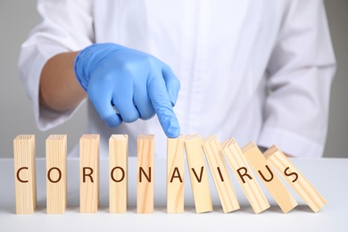 Photo of Doctor stopping domino effect at white table, closeup. Prevent spreading of coronavirus